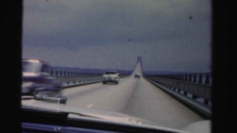 Dashboard footage from 1955 Dade County shows traffic on a long bridge, with one car passing and another ahead on the roadway.