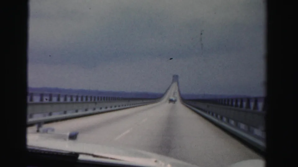 1955 Dade County, Florida home-movie frame from a car crossing a long causeway over water under an overcast sky.
