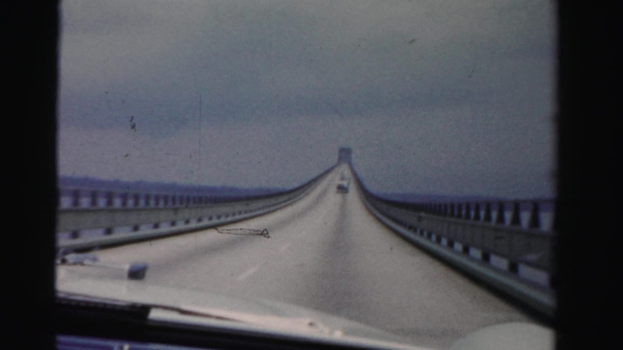 Forward view from a car crossing a long bridge under an overcast sky.