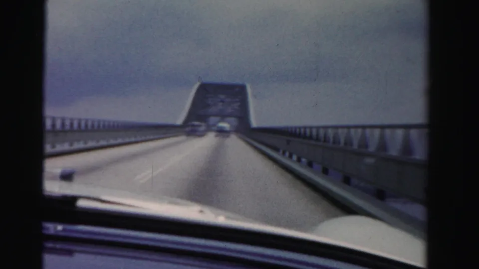 1955 Dade County bridge-crossing frame with two cars ahead, guardrails on both sides, and the filming car hood visible at the bottom.