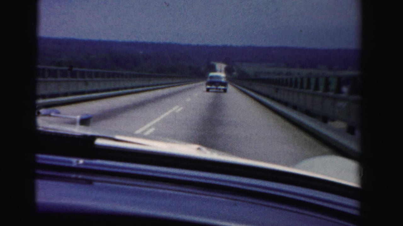 Windshield view of a divided highway with a car ahead and dashboard edge visible.