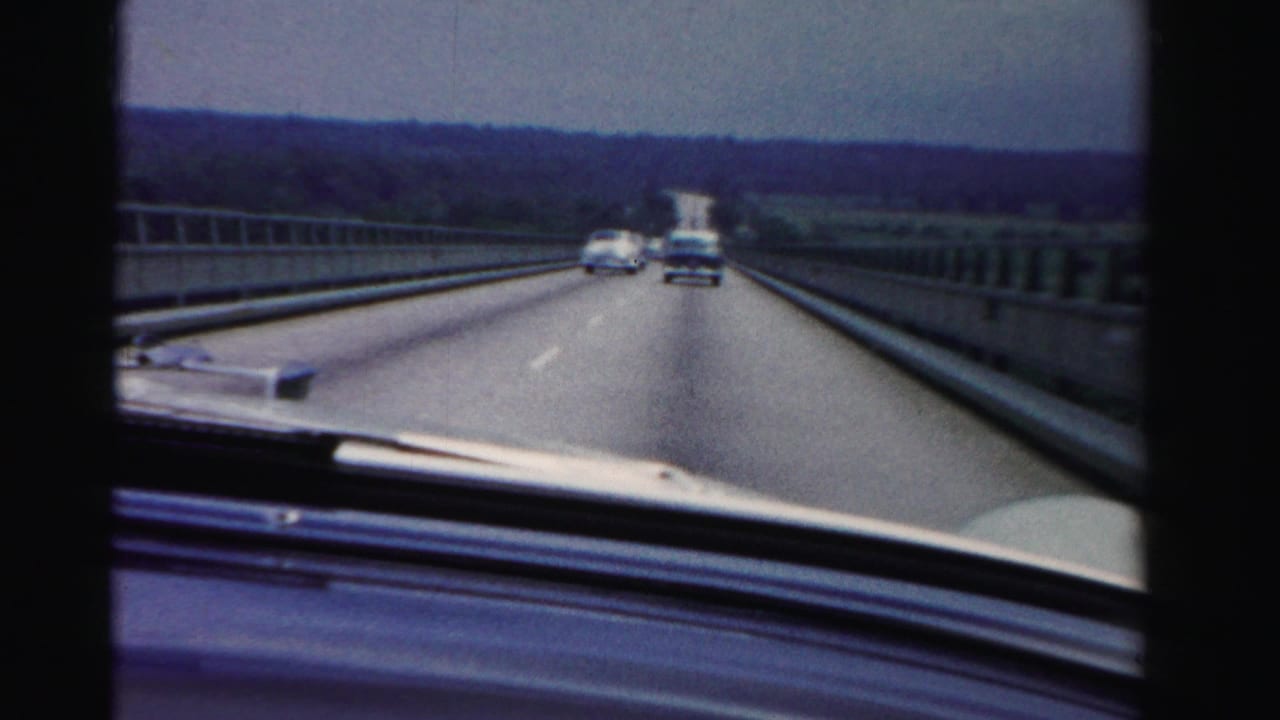1955 Dade County, Florida 8mm windshield view from a moving car crossing a bridge with mid-century vehicles on the road.