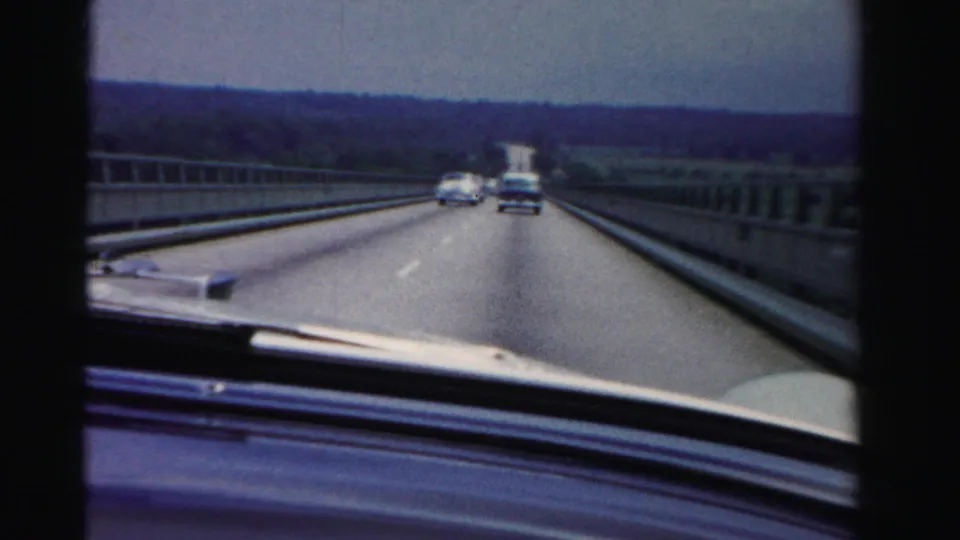 1955 Dade County, Florida 8mm windshield view from a moving car crossing a bridge with mid-century vehicles on the road.