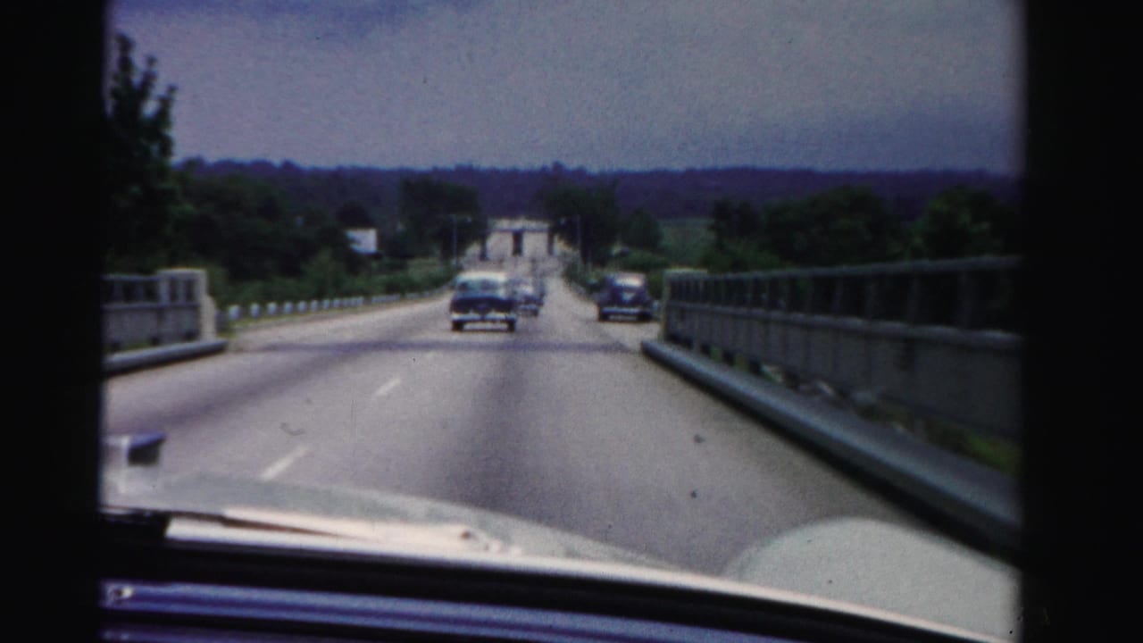 View through a car windshield on a paved bridge or highway with cars ahead.