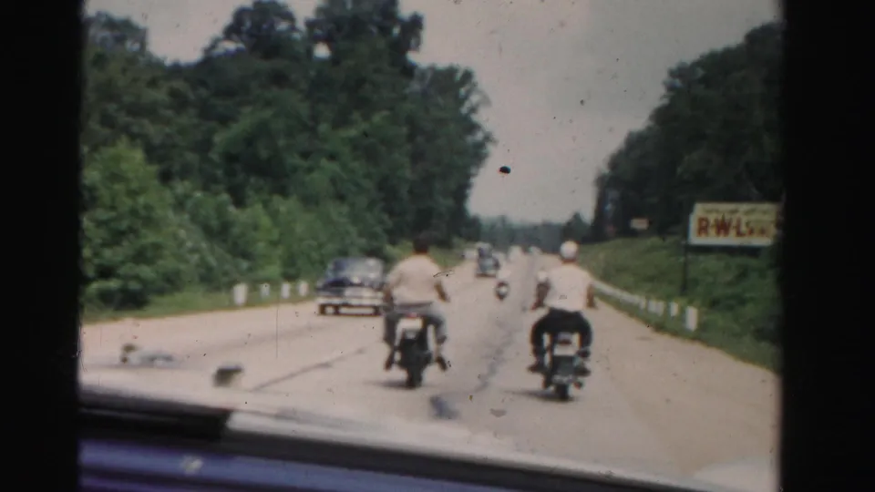 1955 Dade County road scene with two motorcycle riders ahead of the camera car and a dark automobile visible in the left lane.