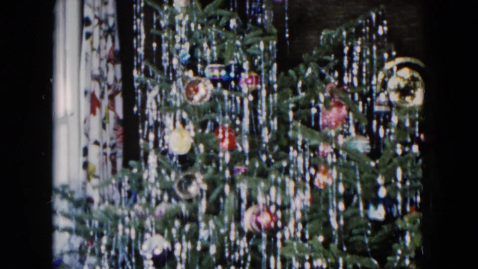 1955 Hicksville frame with a decorated Christmas tree, dense silver lametta, reflective ornaments, and dark room background.