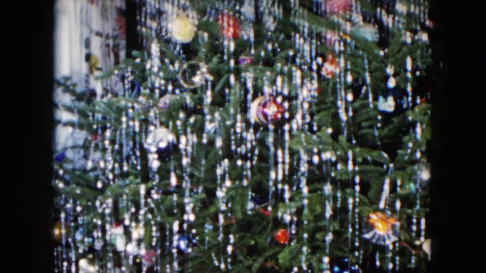 1955 Hicksville frame of a decorated Christmas tree with silver lametta, colored glass baubles, and a dim room background.