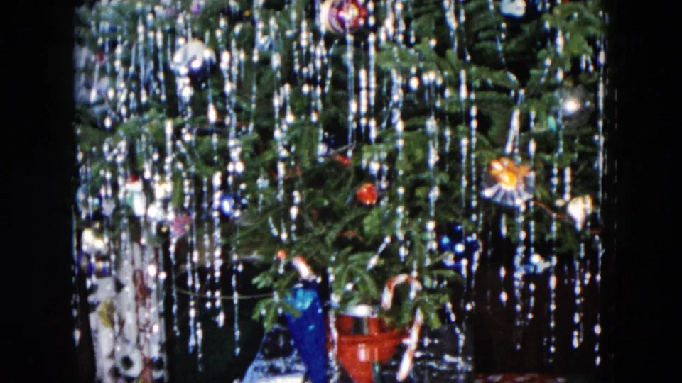 1955 Hicksville frame of a decorated Christmas tree with dense tinsel, colorful ornaments, and lower holiday objects partly visible.