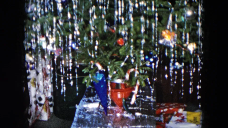 1955 Hicksville home-movie frame showing the lower Christmas tree with tinsel, a blue decorative object, a red pail-like object, and gifts below.