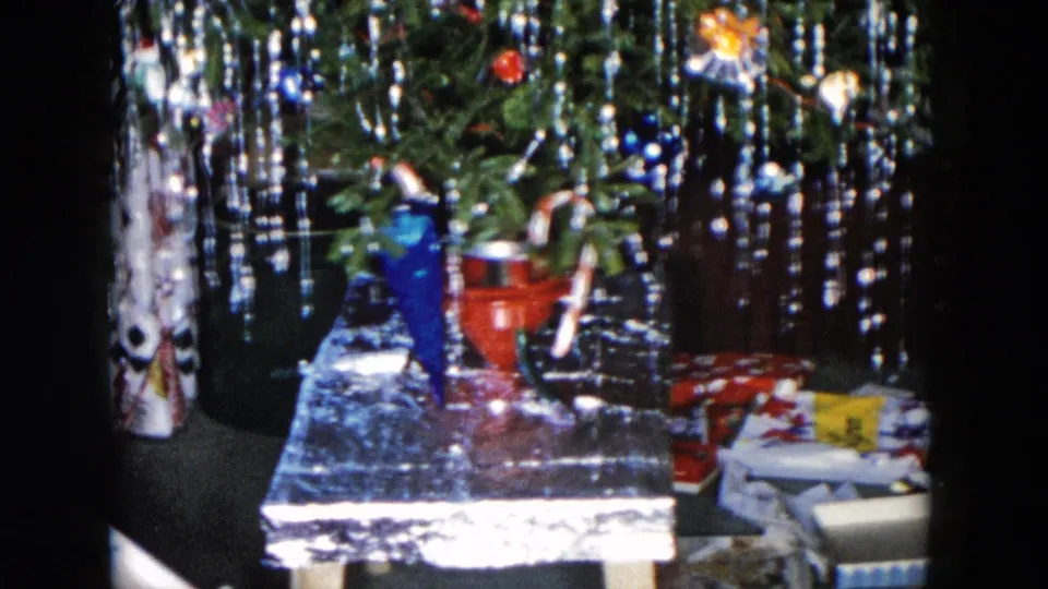 1955 Hicksville frame showing the tree base, dense tinsel, ornaments, a red pail-like object, and wrapped presents beneath the branches.