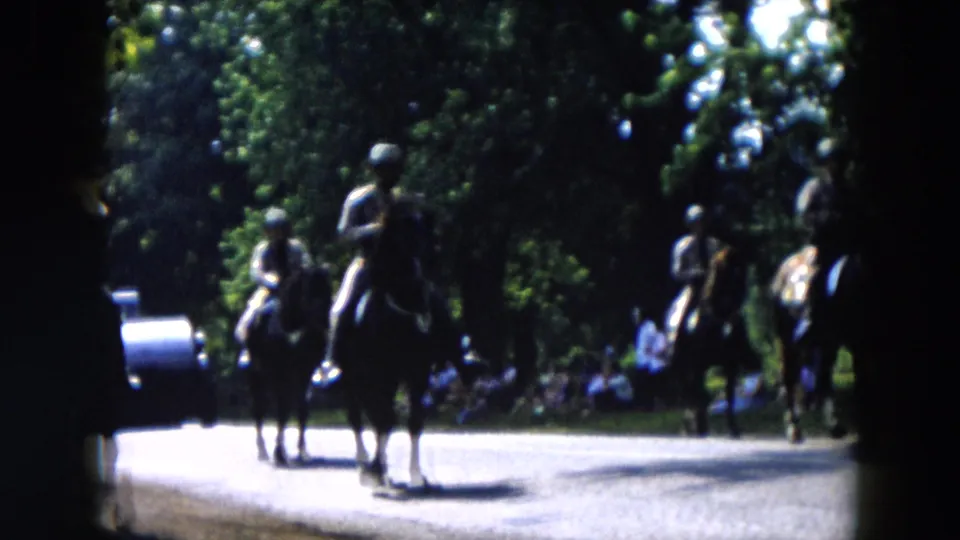A 1955 home-movie view of riders on horseback passing through a sunlit civic parade route in Hicksville.