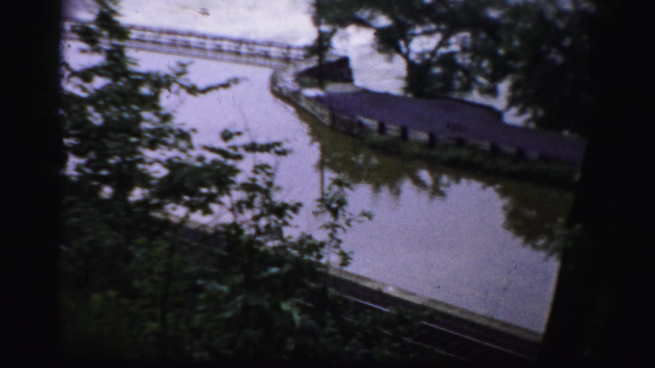 Elevated view of a river edge with trees, a narrow walkway, and water near a dam.