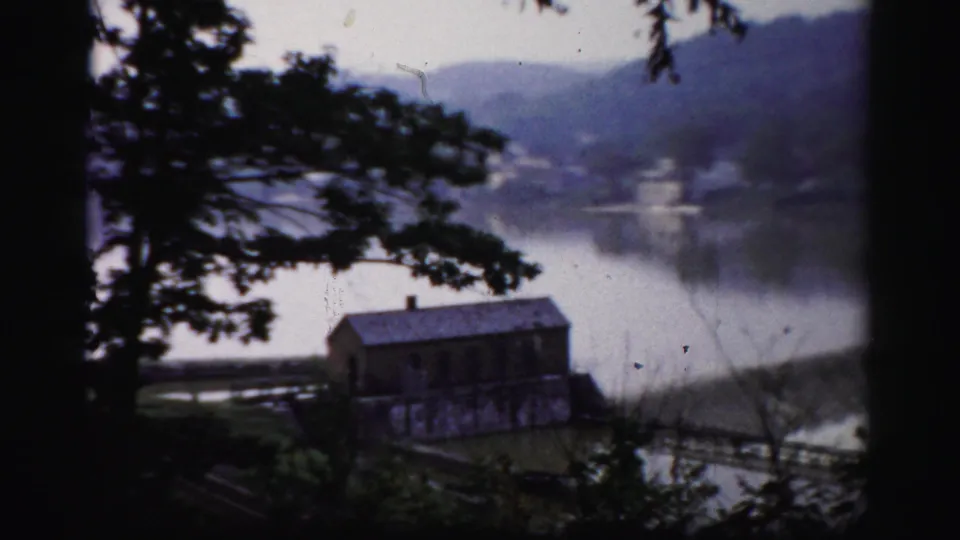 A small building beside the water appears through trees in archival Albany-area lakeside footage from 1956.