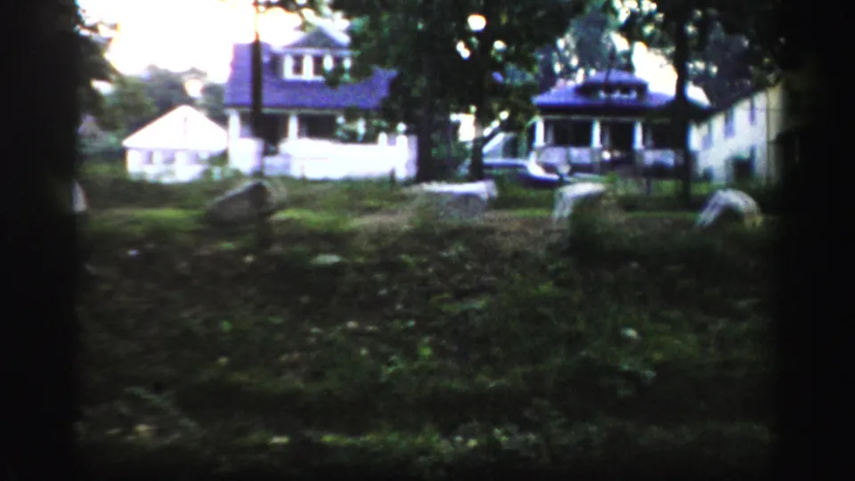 A 1950s Albany-area home-movie frame shows houses, lawns, parked cars, and trees viewed from a shaded yard.