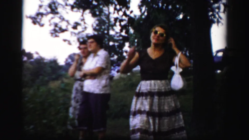 A woman in sunglasses adjusts her hair in a 1950s Albany yard while two adults remain in the background.