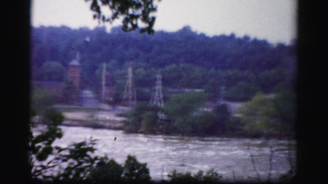 Distant river view with wooded banks, utility towers, and a brick tower beyond the water.
