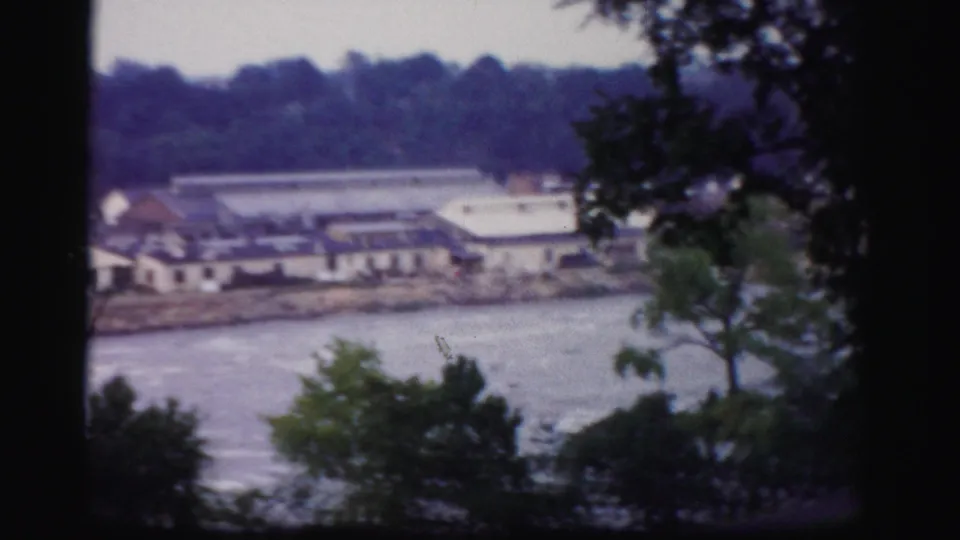 Soft 8mm frame showing the Albany riverfront area, with trees in shadow and industrial structures across the river.