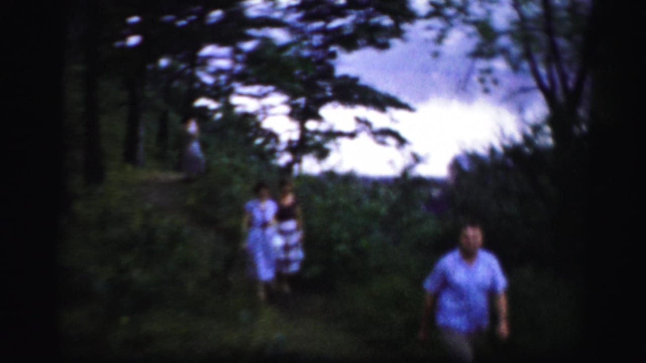 In Albany-area 1950s home-movie footage, three adults walk through a shaded grassy path bordered by trees.