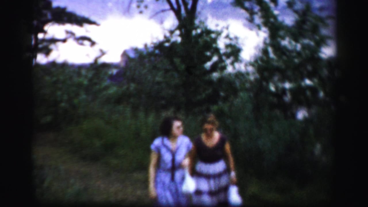 Two adult women in midcentury dresses walk toward the camera on a leafy path in Albany-area 8mm home-movie footage.