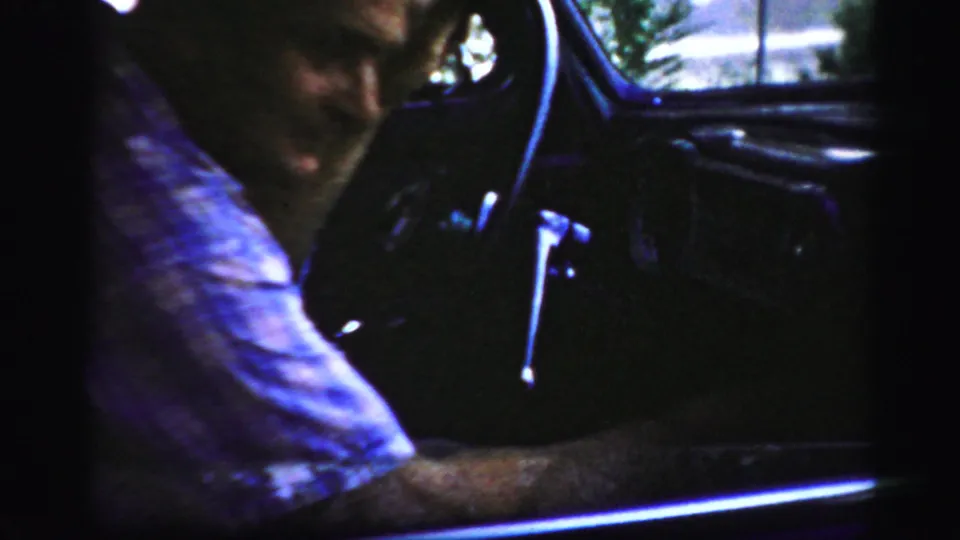 The man remains in the driver's seat of the Albany car interior, his arm extended near the wheel and dashboard area.