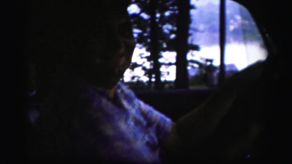 A patterned-shirted man drives through a wooded area, filmed from inside the car in 1950s Albany-area home-movie footage.