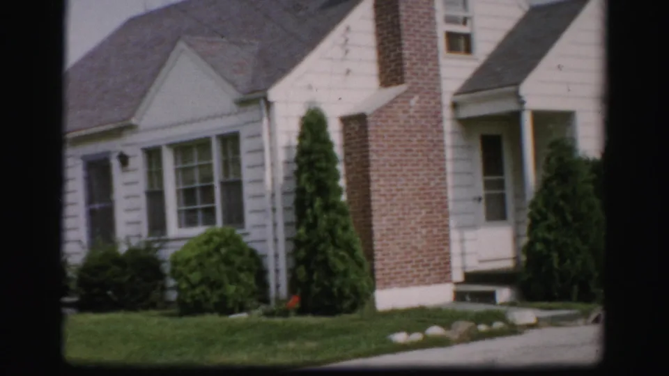 1956 Albany frame with the house front, brick chimney, shaded entry, multi-pane windows, shrubs, and lawn in sunlight.