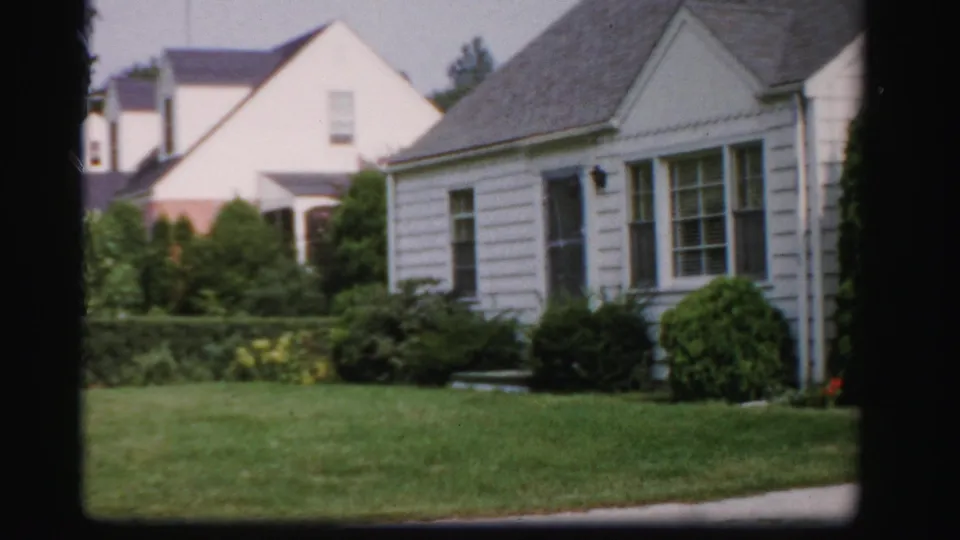 1950s Albany residential exterior with white siding, gray roof, trimmed shrubs, lawn, and neighboring houses.