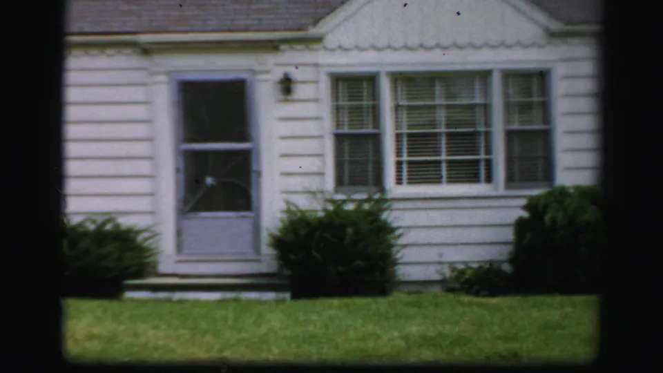 Closer 1950s Albany house exterior showing white siding, a screen door, front windows, shrubs, and lawn.