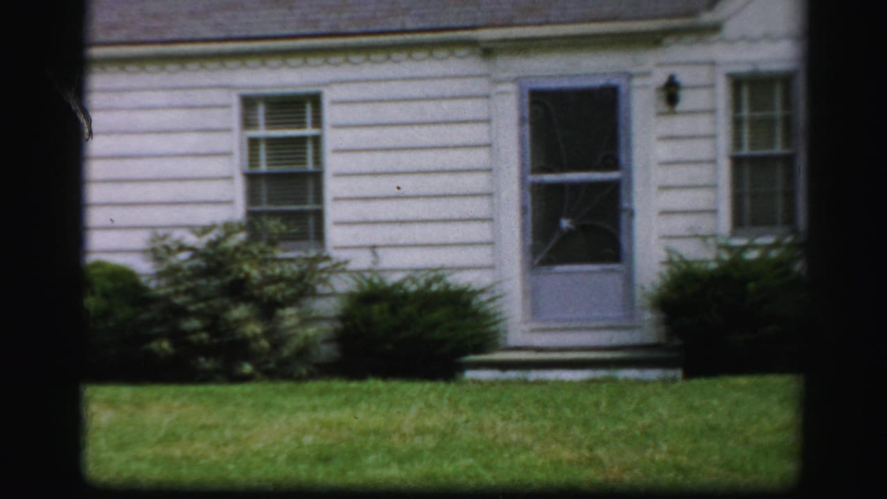 White clapboard house with screen door, front windows, shrubs, and green lawn.