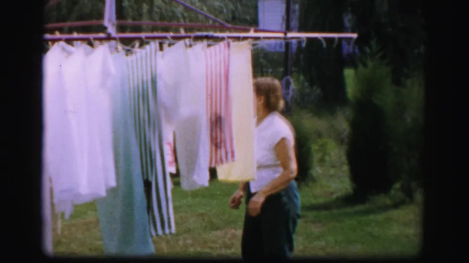 A woman in a white blouse stands next to hanging laundry on a rotary clothesline in Albany, New York home-movie footage.