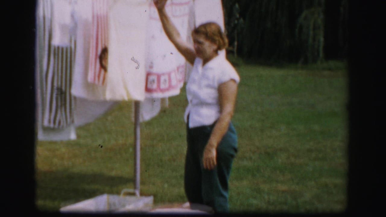 Woman standing beside laundry hanging on a clothesline in a grassy yard.