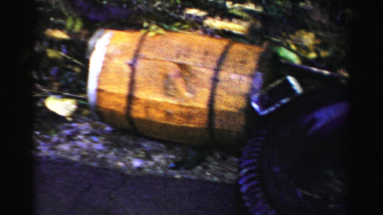 Wooden barrel near floodwater with the edge of a dark car at right.