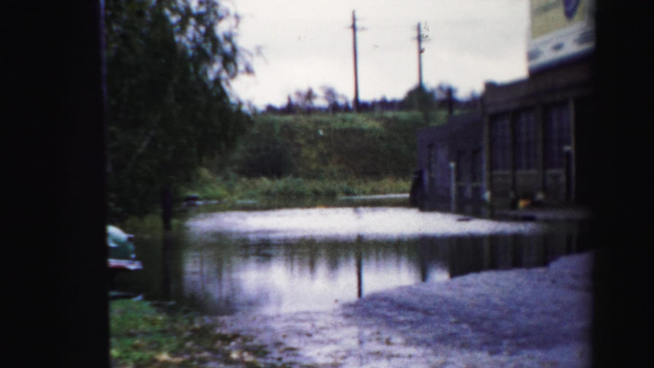 Floodwater beside a low commercial building with utility poles and a large sign above the roofline.