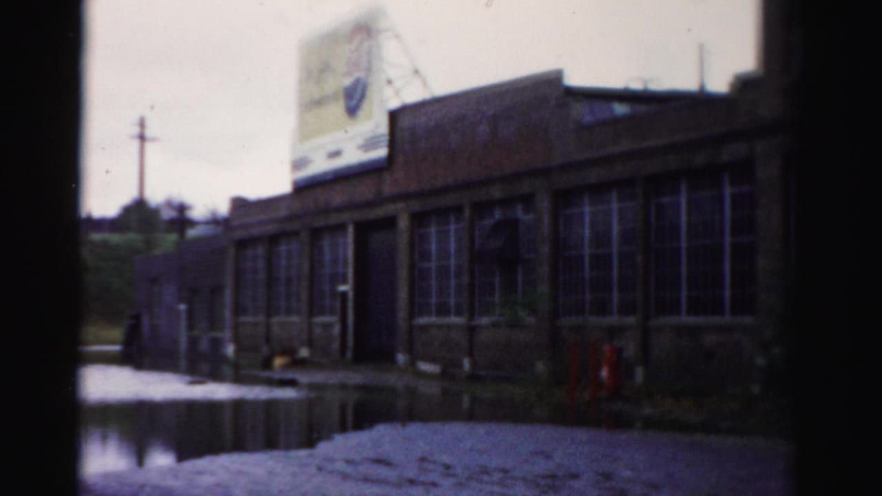 Floodwater beside a brick industrial building with a faded rooftop sign and dark frame edges.