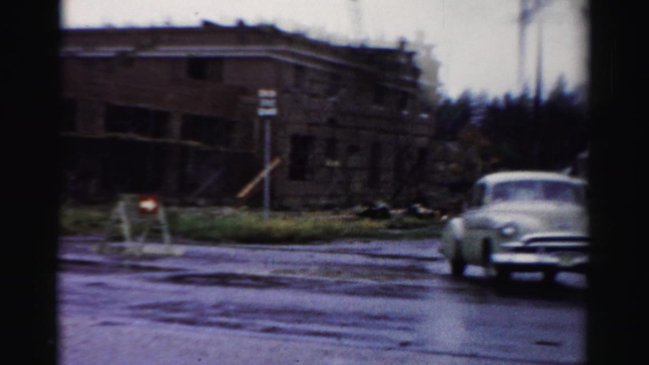Car turning on a wet corner beside a brick building under construction.