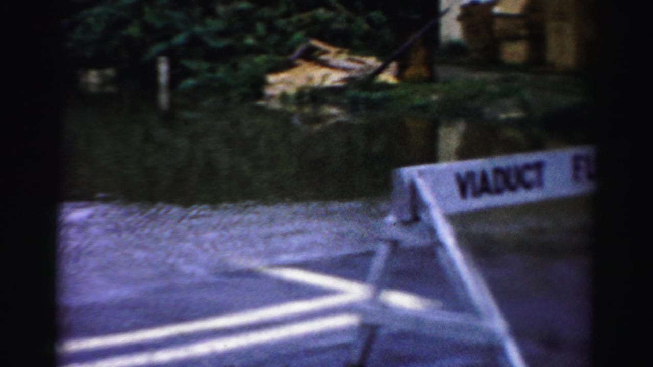 Albany, New York 8mm frame showing a white VIADUCT FLOODED barricade near standing water, roadside vegetation, and wet pavement.