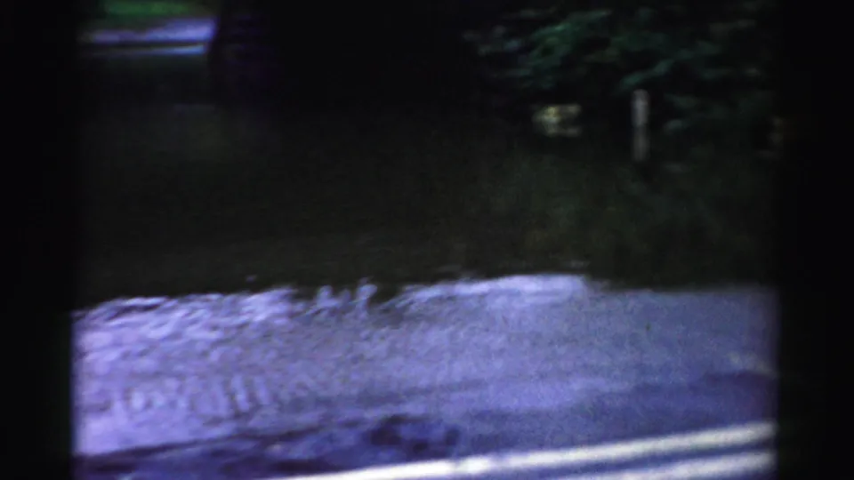 Albany 8mm frame with standing floodwater across a roadway, dark overhead structure, wet pavement, and dim reflected light.