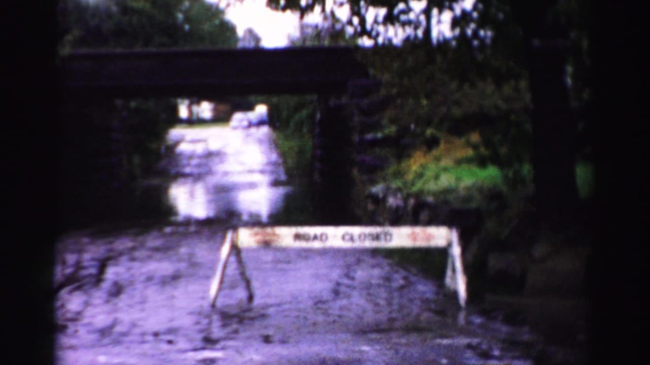 Flooded road blocked by a ROAD CLOSED barricade beneath a low stone bridge.