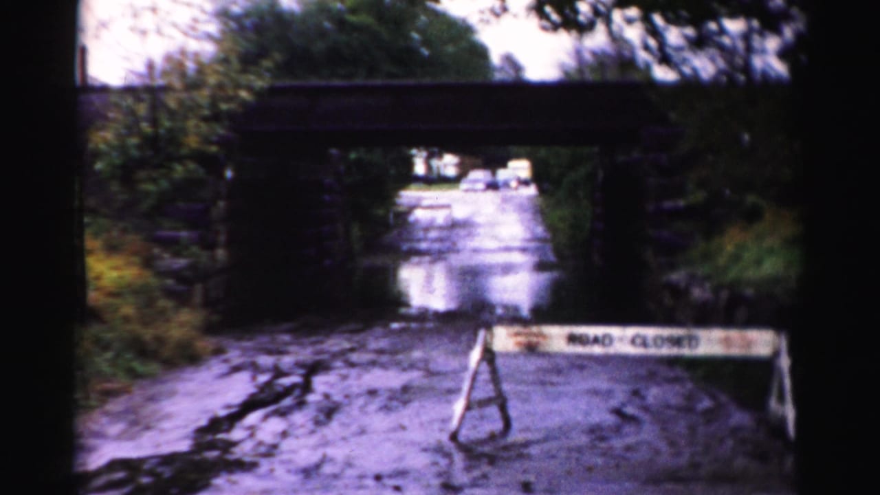 ROAD CLOSED barricade stands in front of floodwater passing under a stone bridge.