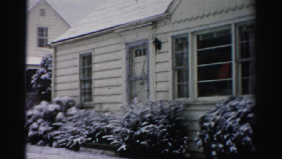 1956 Albany home-movie view of the front entry and window of a light clapboard house after snowfall.