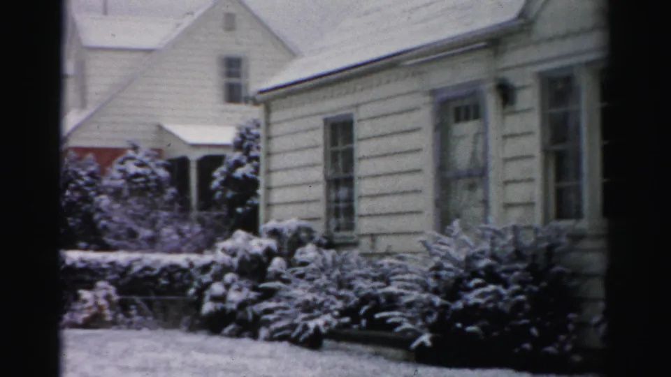 1956 Albany frame showing the snowy house exterior and part of a neighboring building in a residential winter setting.