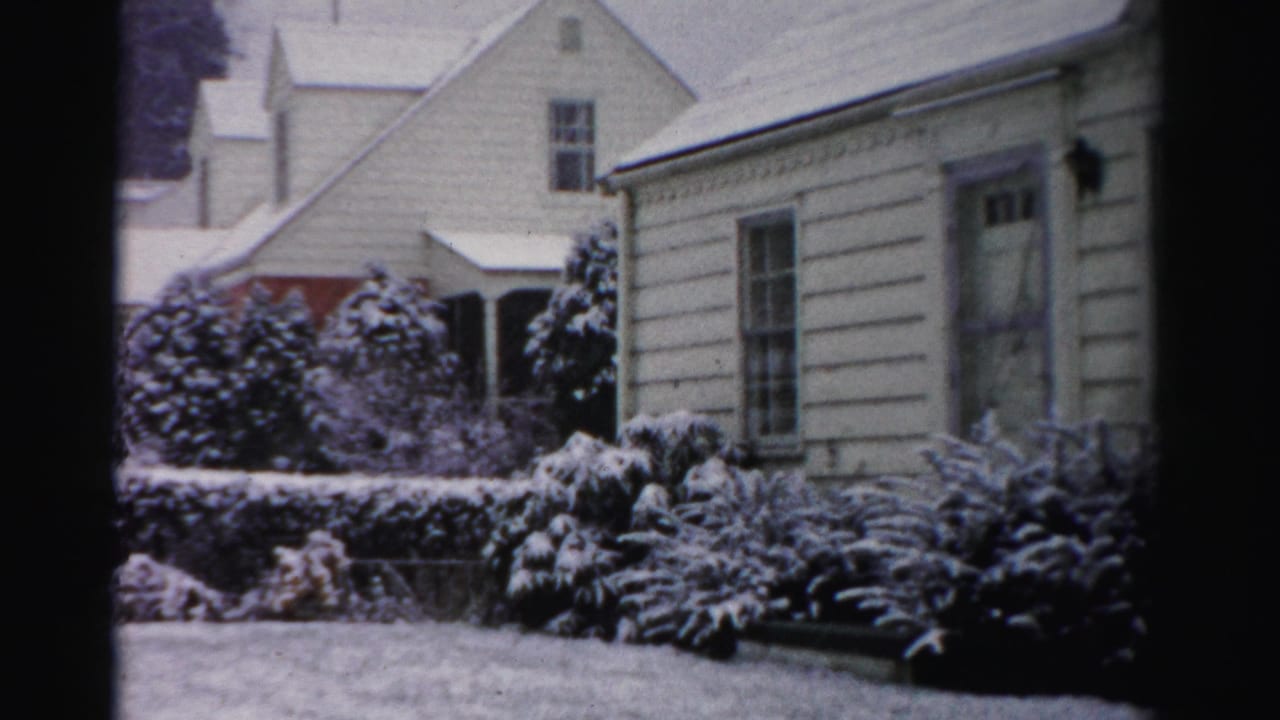 1950s Albany home-movie frame showing a white house, bare trees, and shrubs blanketed by fresh snow.