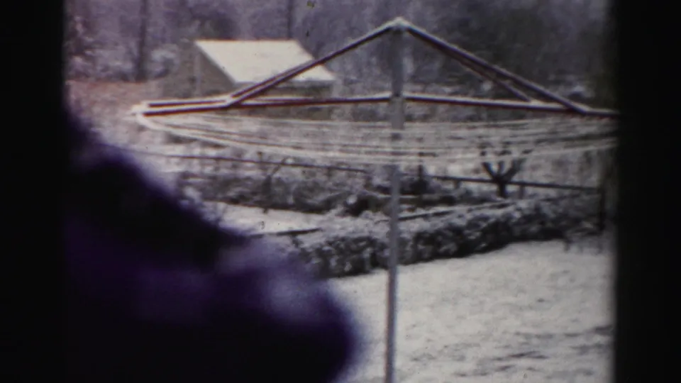 1950s Albany home-movie frame showing a snow-covered yard through window framing, with a clothesline and dark foreground shape.