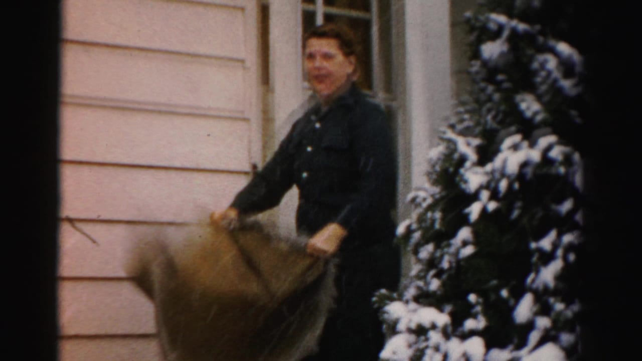Adult woman smiles toward the camera on a snowy residential porch in Albany-area 1956 home-movie footage.
