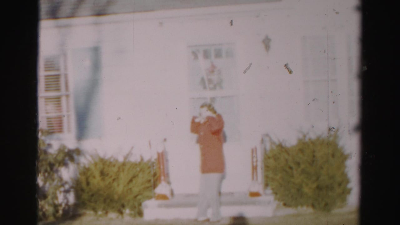 Woman in a red jacket stands on front steps near a white door and shrubs.
