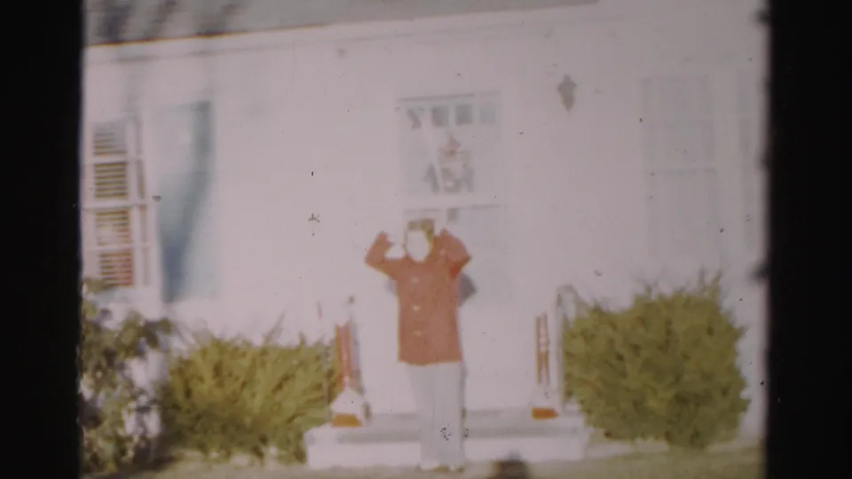 The woman stands centered on the steps of the Albany house, both hands raised as she adjusts a hood or head covering.