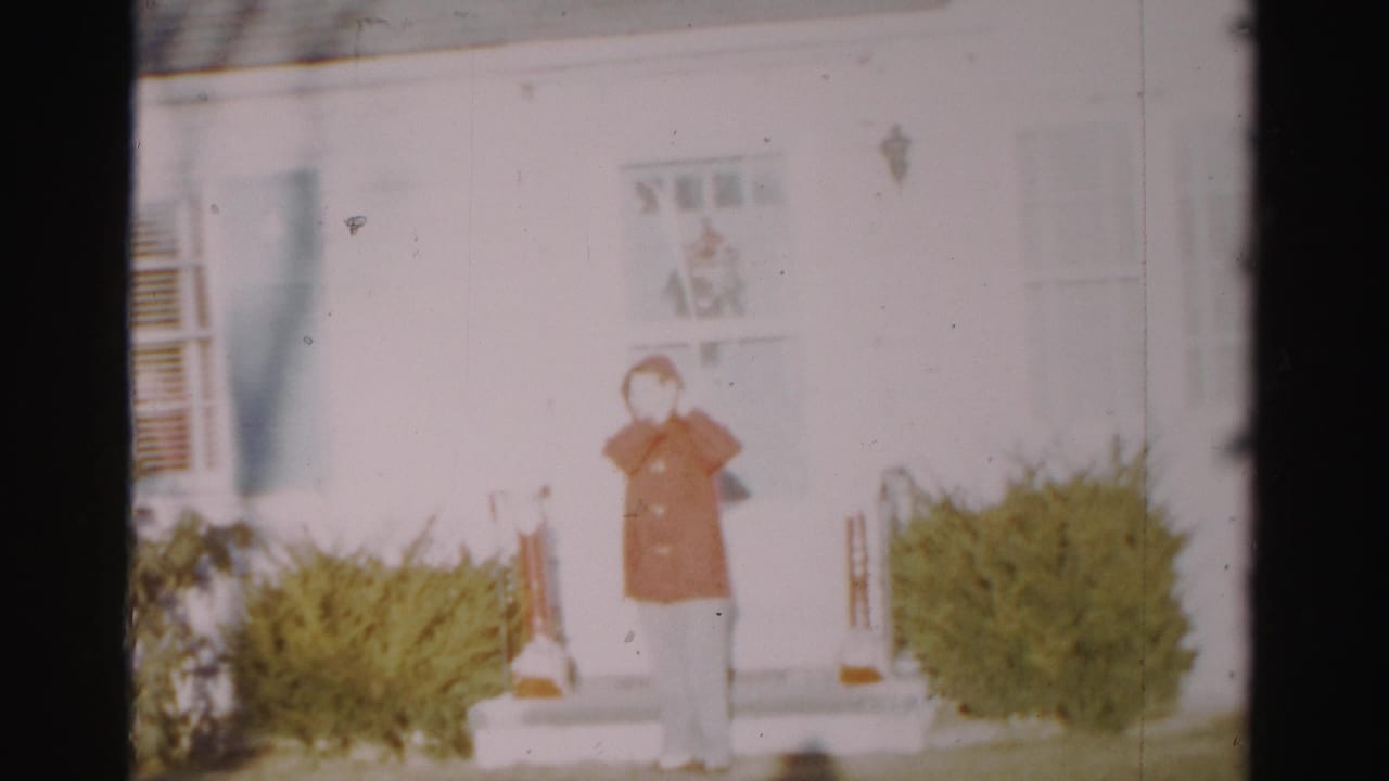 A soft 8mm frame shows the woman on the house steps in Albany, hand near her face after adjusting her head covering.