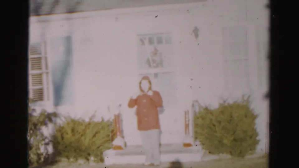 The woman stands outside the Albany home in a red jacket and light pants, framed by a white door, steps, porch light, and shrubs.