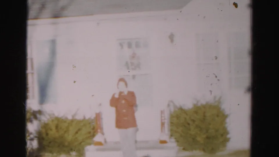 The adult remains outside the white house in Albany, wearing orange hooded outerwear against a snowy residential setting.