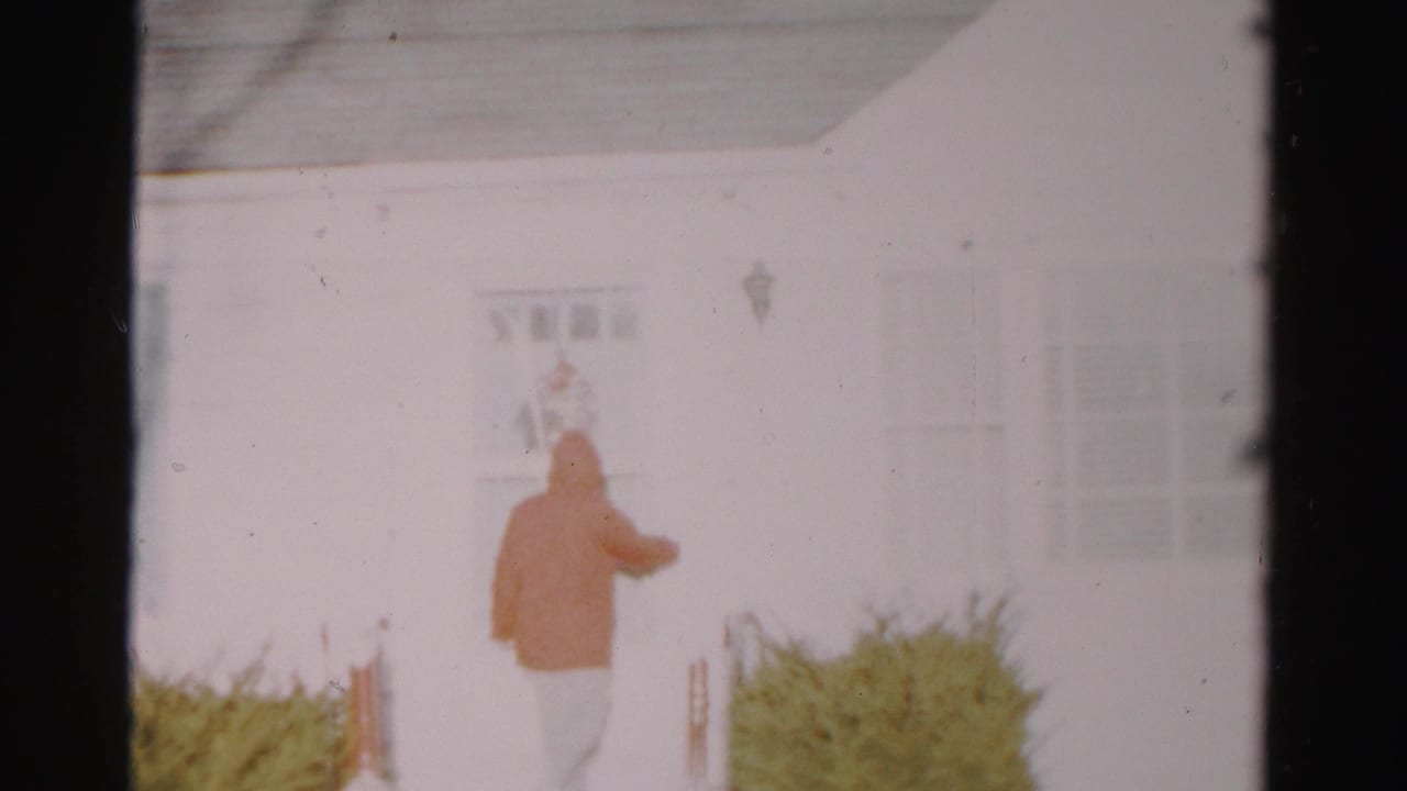 In Albany home-movie footage from 1956, a hooded person approaches the front door of a white suburban house.